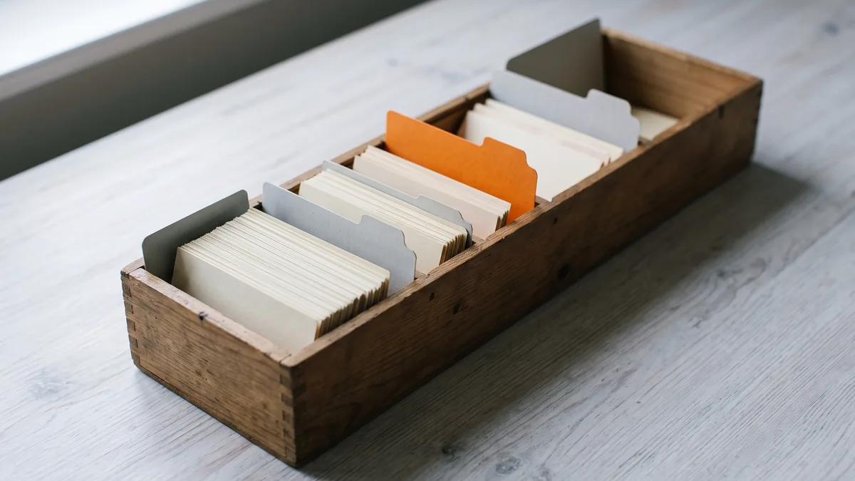 Una caja de madera alargada con tarjetas de repaso repartidas en compartimentos por separadores grises, uno de ellos naranja.